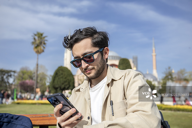 一名年轻男子在土耳其伊斯坦布尔的圣索非亚大教堂前看手机图片素材