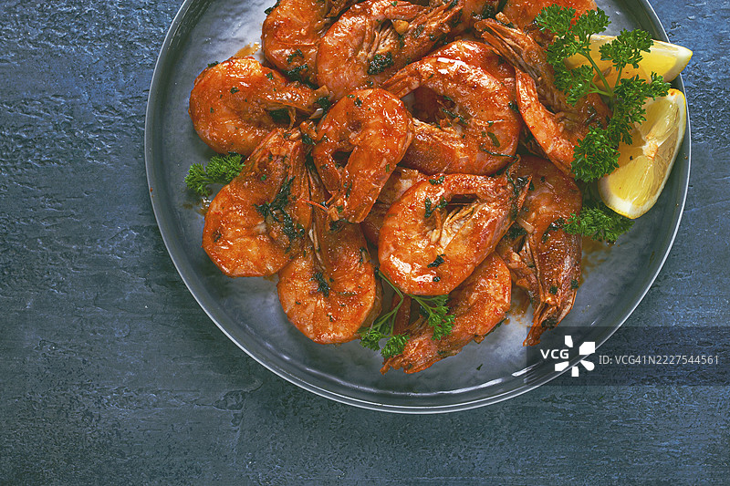 炸白脚虾和老虎虾放在碗里，配有柠檬和香草，背景为蓝色图片素材