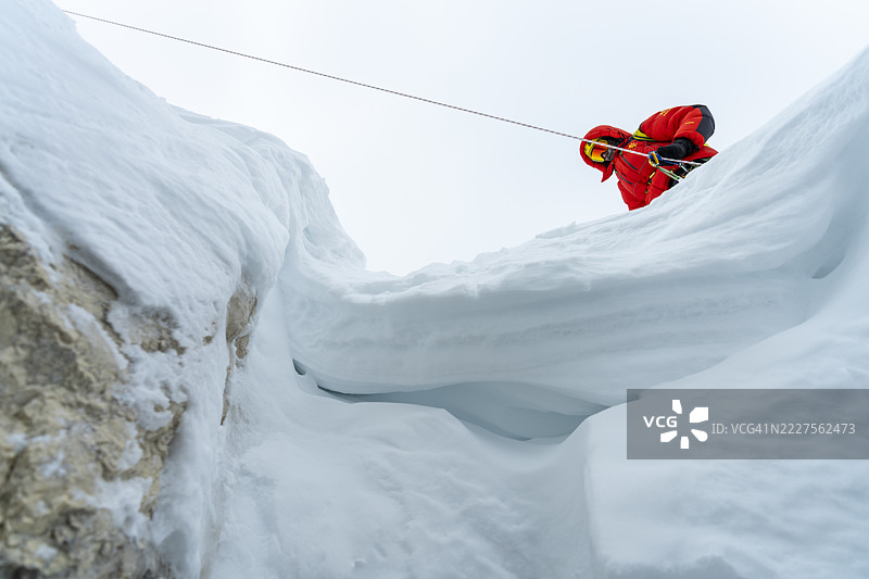 穿着红色夹克的登山者在高海拔地区用安全绳攀爬雪脊图片素材
