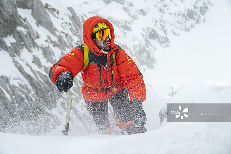 中年男性登山者穿着明亮的橙色高海拔装备攀登雪坡图片素材