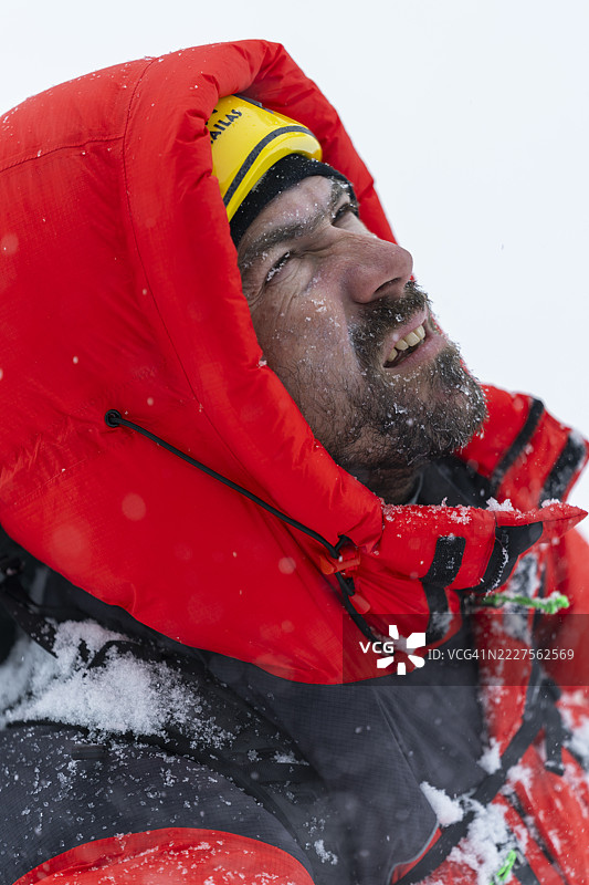 中年登山者穿着红色冬季夹克，在阿尔卑斯探险中勇敢面对大雪图片素材
