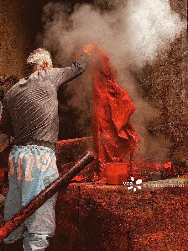 男子在土耳其阿克萨赖从锅中准备红色染料布的背影图片素材