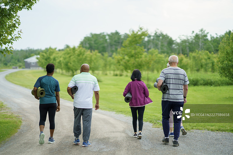 一群成年人在阳光明媚的日子里享受户外散步，带着健身垫图片素材