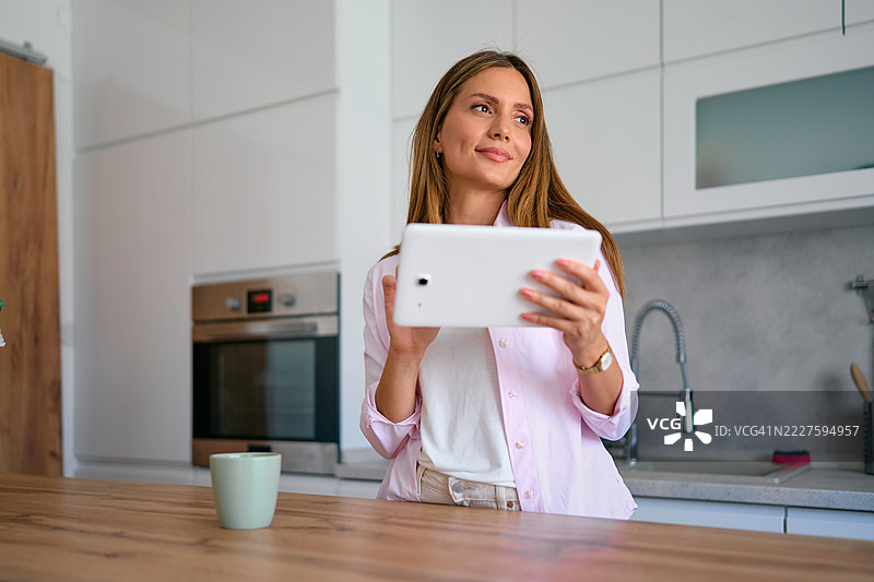 女人在厨房使用平板电脑并向一旁看去图片素材