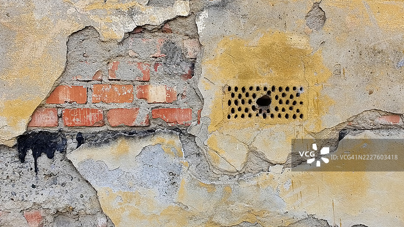 老旧的通风口铁格栅，位于破损的砖墙和灰泥墙上图片素材