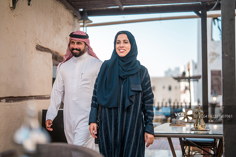 微笑的阿拉伯夫妇穿着传统服饰走过历史悠久的阿尔巴拉德餐厅环境图片素材