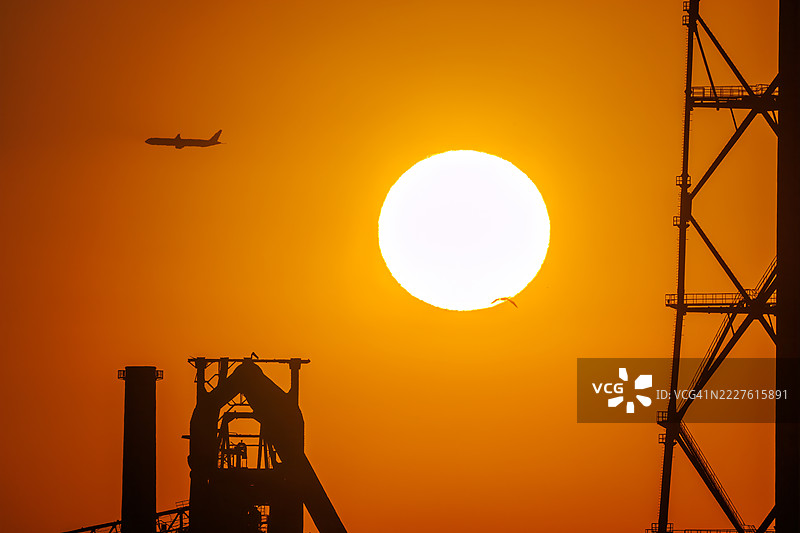 第一缕阳光与一架客机和鸟的剪影。它即将降落在附近的羽田机场。第一缕阳光越过运河对岸的烟囱和电厂、钢铁厂。图片素材
