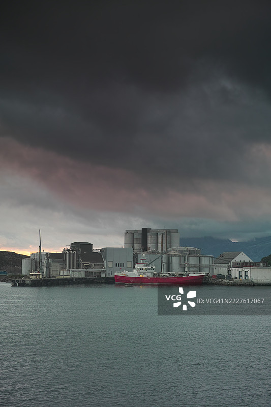 工业港口场景，货船停靠在戏剧性的暴风雨天空下，展现海洋和城市的氛围图片素材