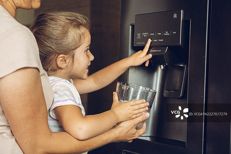 智能冰箱。妈妈和孩子从制冰机中装冰块。图片素材