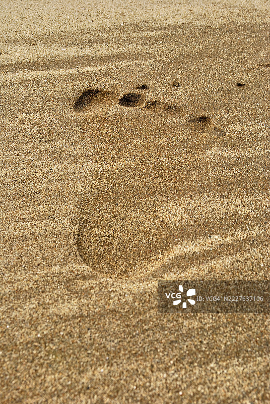 一只脚印印在浅棕色的沙子上，显示出脚的形状和脚趾的痕迹。图片素材