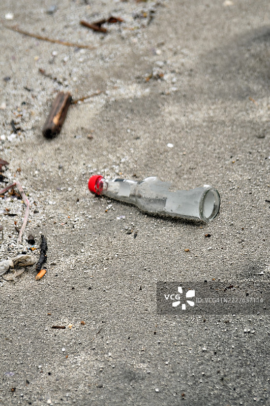 一个带红色瓶盖的透明玻璃瓶倾斜地躺在沙地上。图片素材