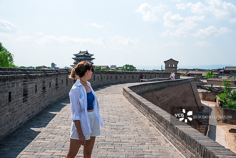 年轻女性在阳光明媚的日子里享受在平遥城墙上散步。图片素材