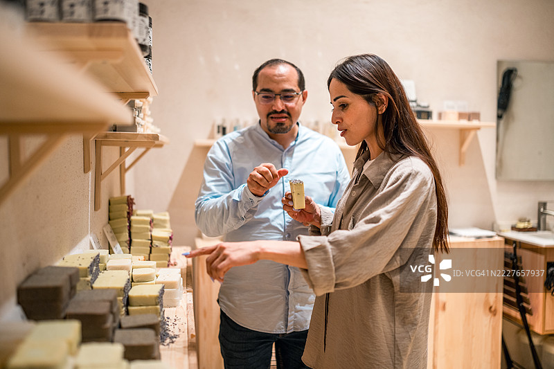 年轻女性游客在阿尔巴拉德商店购买传统香皂，温暖的室内灯光照耀。图片素材