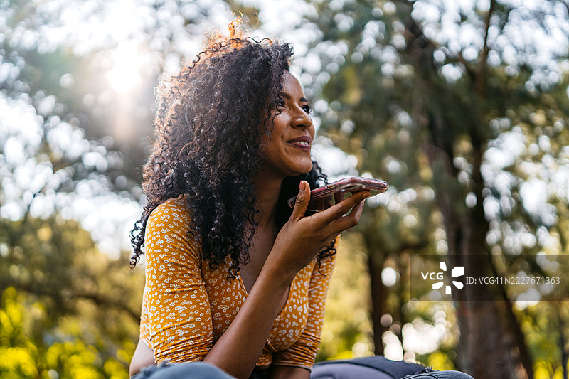 年轻的西班牙裔女性在阿根廷布宜诺斯艾利斯的公共公园里坐着，用手机发送语音信息图片素材