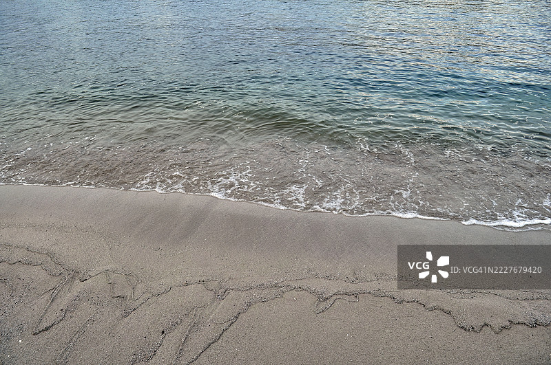 沙质表面显示出潮湿的、较暗的区域，表明水的流动。图片素材