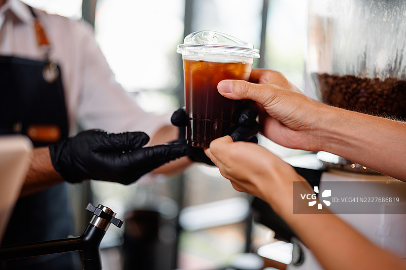 咖啡师将一杯外带冰咖啡递给顾客的特写镜头。图片素材