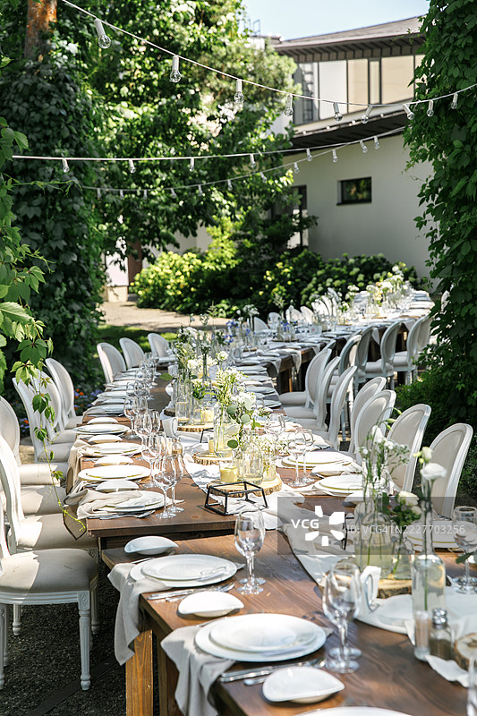 一个精美布置的户外餐桌，装饰着精致的花朵和椅子，背景是一个花园。图片素材