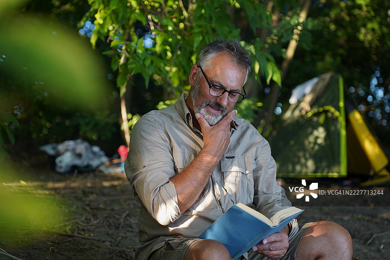 中年男子在森林中阅读、喝咖啡和露营图片素材