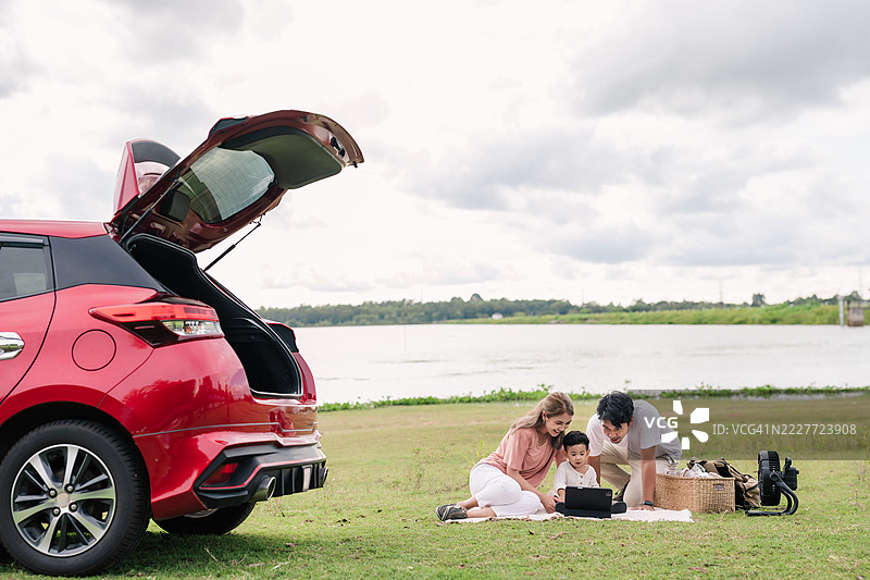 现代家庭在湖边野餐，红色SUV和平板电脑图片素材