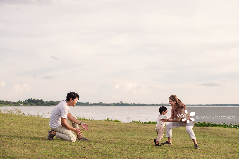 亚洲家庭在河边享受户外时光。一个小男孩高兴地跑向他的母亲，而父亲在一旁注视，捕捉着自然中爱的瞬间、亲密的联系和积极的家庭互动。图片素材