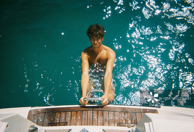 年轻男子游泳后爬上船，模拟胶卷效果图片素材