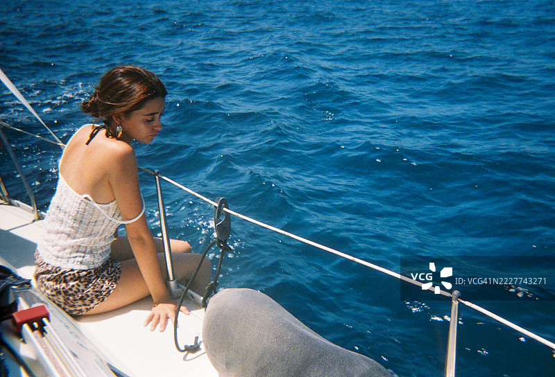 年轻女性坐在帆船上，静静地望着海面，享受宁静的夏日下午。胶卷效果。图片素材