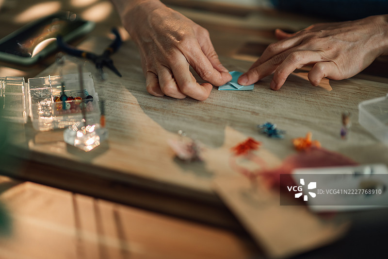 工匠在木桌上用彩色纸制作折纸首饰图片素材