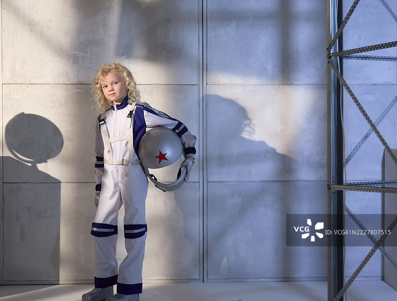 全身肖像。金发女孩宇航员站着，手里拿着宇航员头盔。图片素材