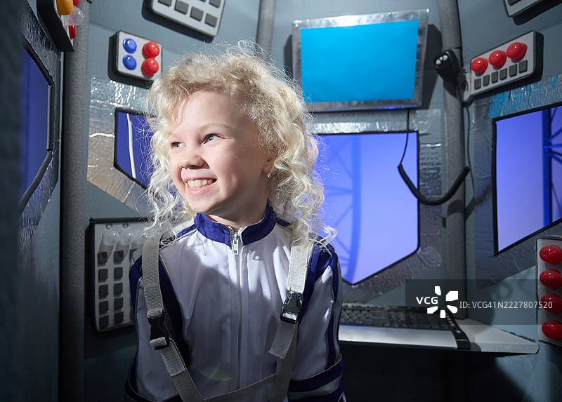 特写肖像。可爱的女孩宇航员坐在飞船控制舱内，凝视着火箭舷窗。图片素材