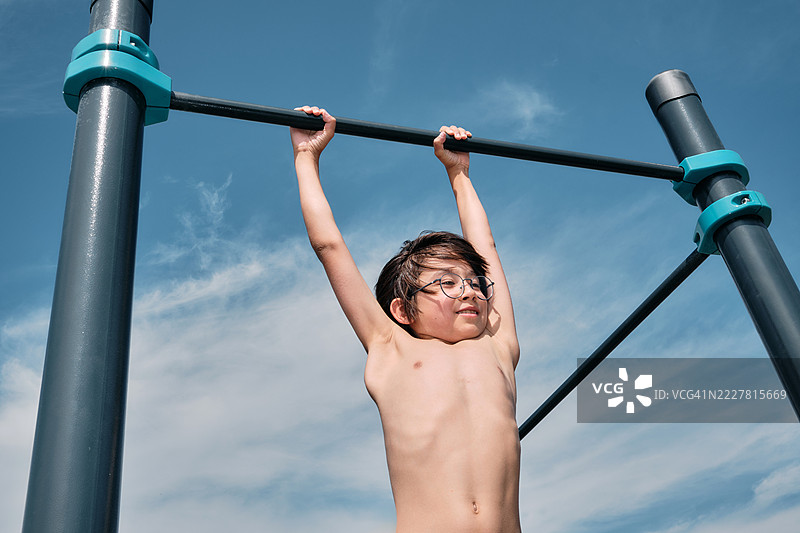 一个韩国男孩在运动场的单杠上悬挂，背景是天空。图片素材