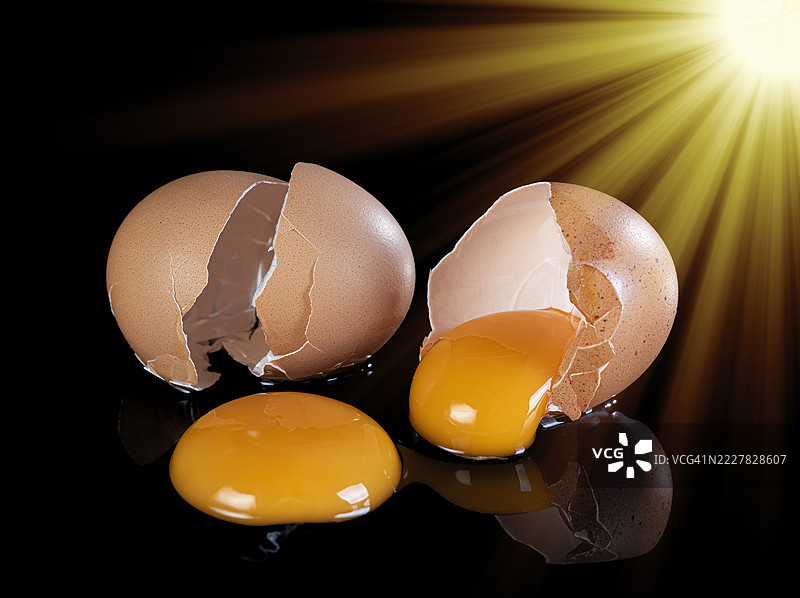 两只破碎的鸡蛋，蛋黄流出，背景为黑色，照亮的光线射入。图片素材