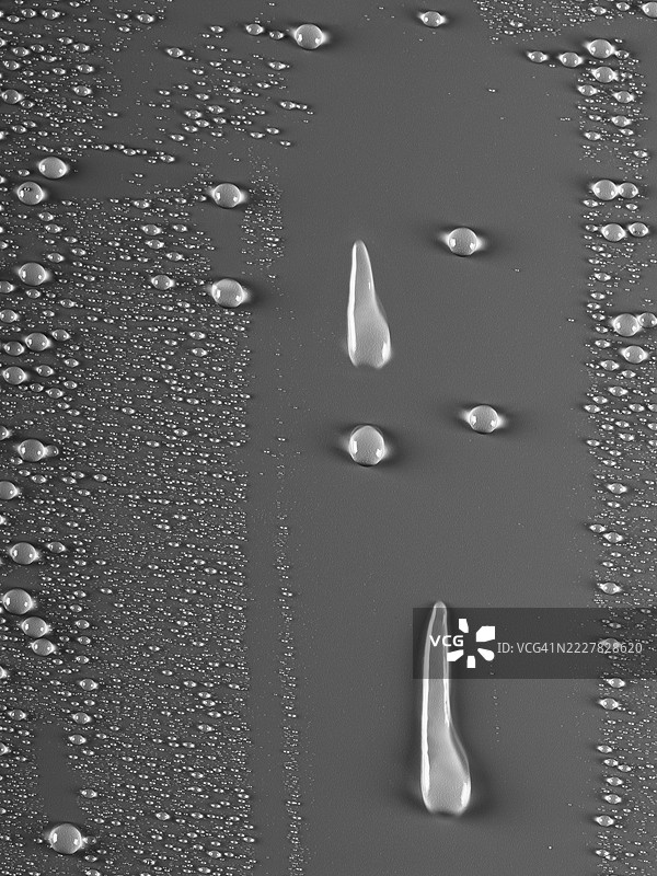 两滴清水从湿润的灰色表面上滑落并滑下。图片素材