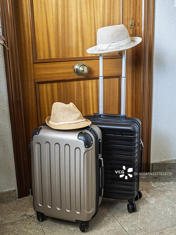 两个随身行李箱和两顶帽子放在公寓的入口门旁。图片素材