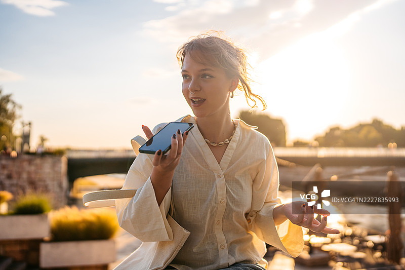 年轻女性坐在码头边用手机发送语音消息图片素材