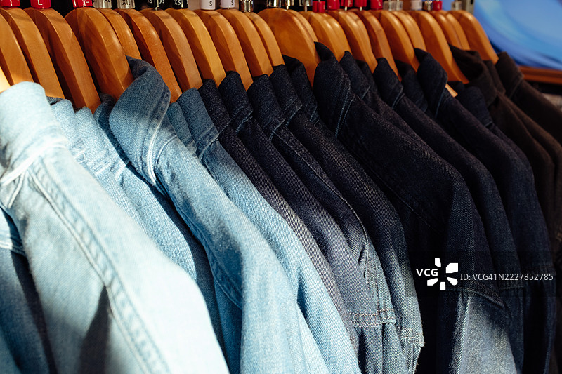商店里挂着不同蓝色阴影的牛仔衬衫，悬挂在木制衣架上图片素材