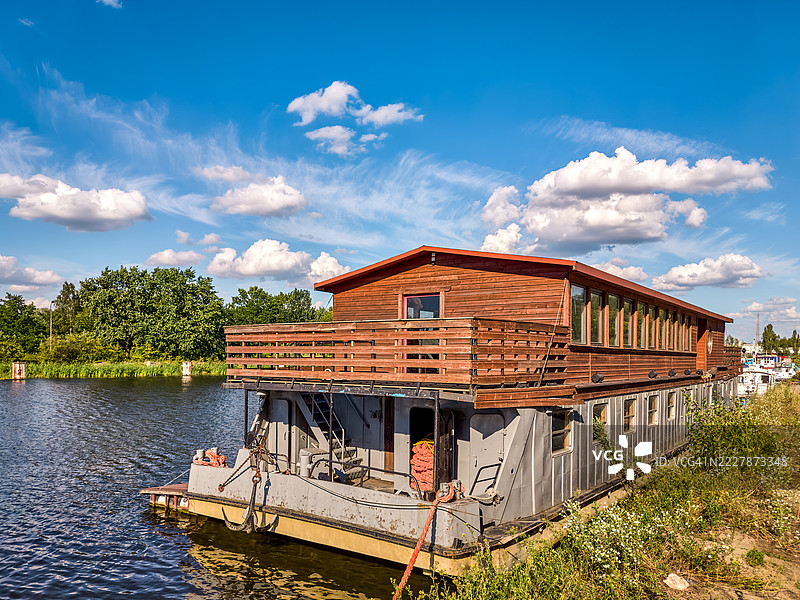 一艘乡村风格的房屋般的船停靠在草坪边。图片素材