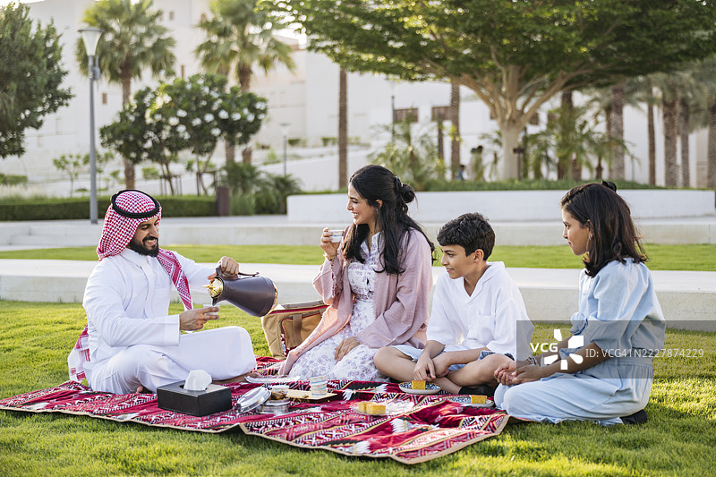 沙特父亲在吉达文化广场的野餐毯上为家人倒传统茶图片素材