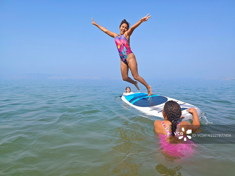快乐女孩在夏日从立式划水板上跳起，做出和平手势。图片素材