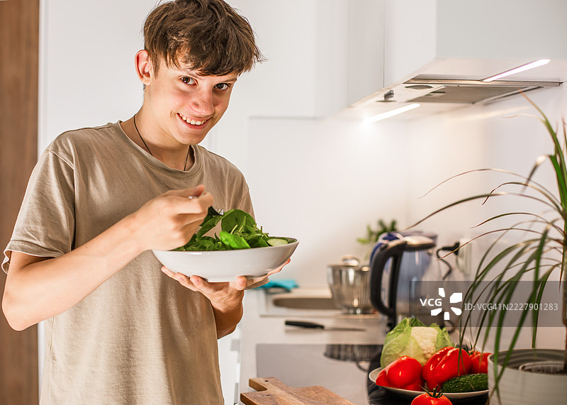 快乐的少年在厨房里准备了一份新鲜蔬菜的素食沙拉图片素材