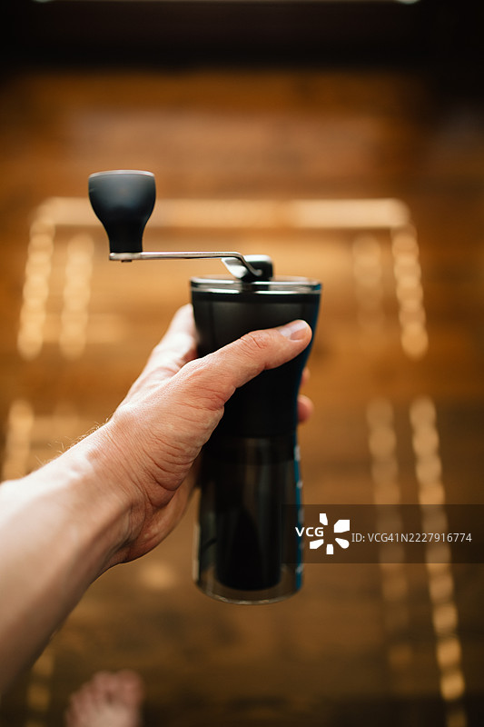 手握手动黑色咖啡磨豆机，背景为木地板的家居环境图片素材