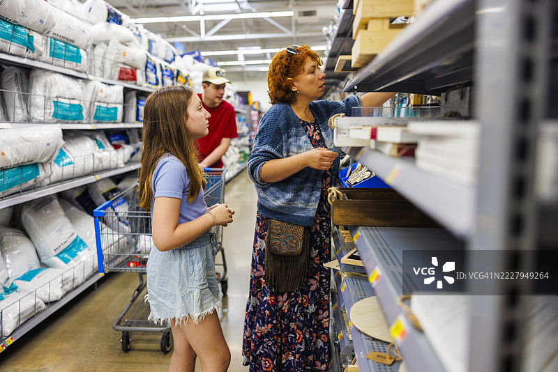 浏览家庭必需品。中年母亲和年轻女儿在商店过道一起购物。图片素材