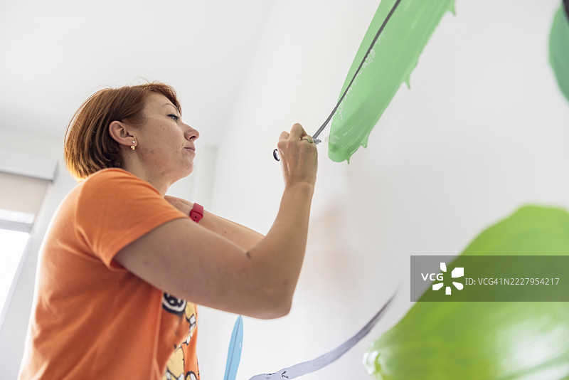 家居室内创意与设计。创意女性艺术家在晨光中在白墙上绘制线条和笔触。低角度拍摄。图片素材