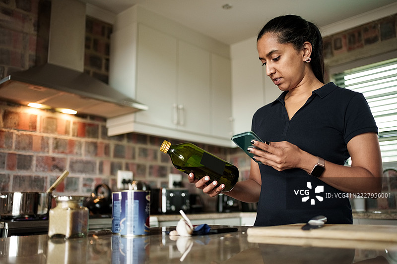 女性在现代厨房中使用智能手机并手持橄榄油图片素材