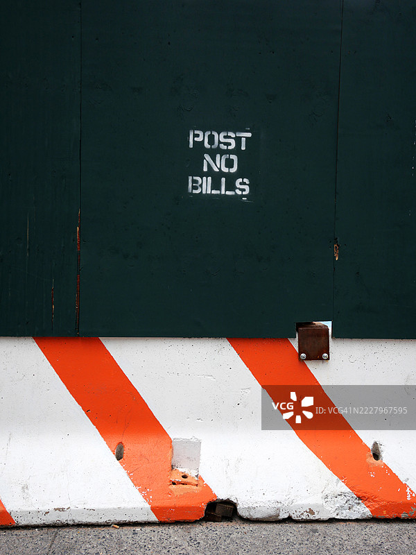 绿色木板和涂有红线的白色混凝土块制成的施工围栏特写。“禁止张贴广告”字样为喷涂。水泥人行道。美国纽约州曼哈顿。图片素材