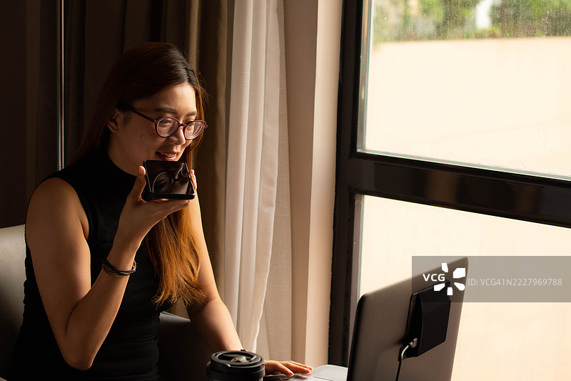 一位中年千禧一代的东南亚女性在家中无缝使用智能手机和笔记本电脑——通过用户友好的应用程序和平台检查余额、进行交易和管理预算。图片素材