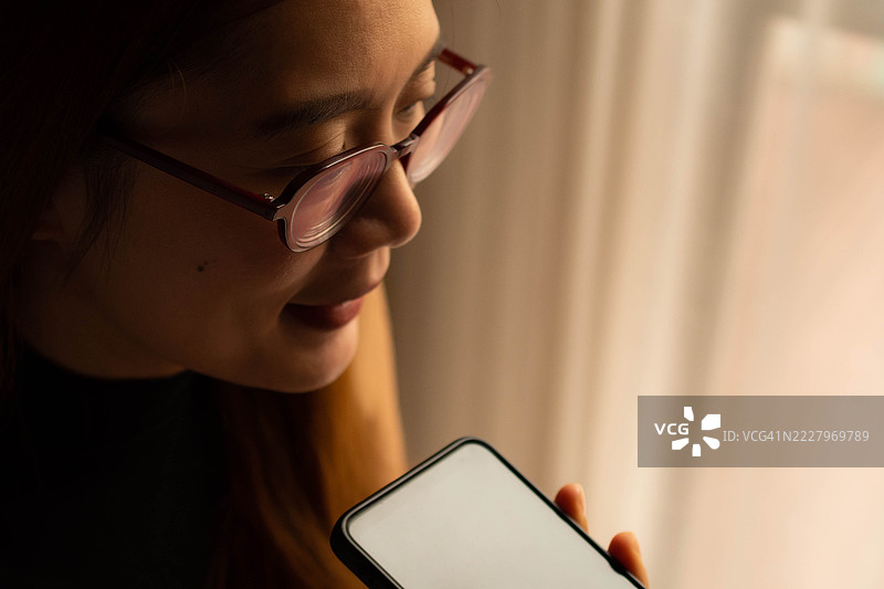 一位中年千禧一代的东南亚女性在家中使用智能手机——通过用户友好的应用程序和平台检查余额、进行交易和管理预算。图片素材