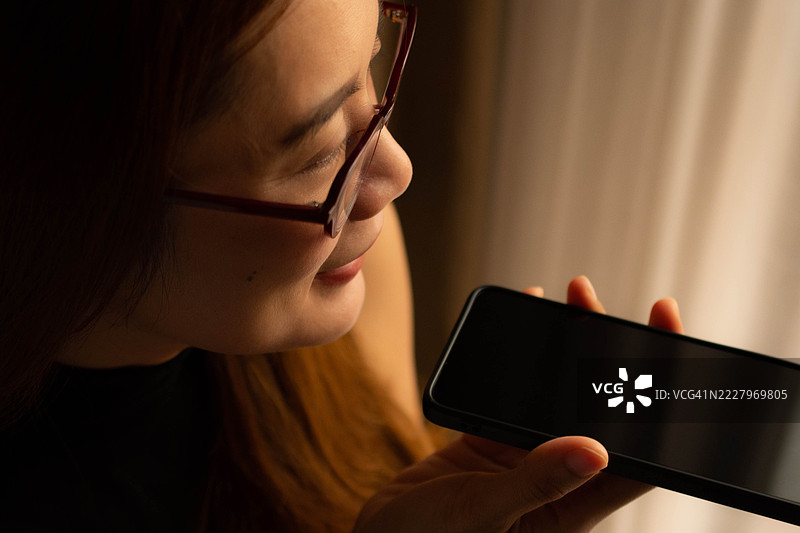 一位中年千禧一代的东南亚女性在家中使用智能手机——通过用户友好的应用程序和平台查看余额、进行交易和管理预算。图片素材