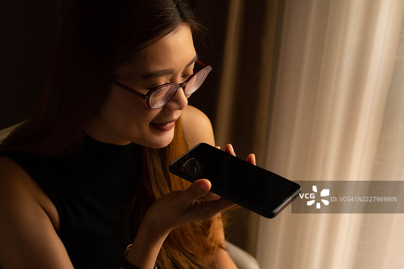 一位中年千禧一代的东南亚女性在家中使用智能手机——通过用户友好的应用程序和平台检查余额、进行交易和管理预算。图片素材
