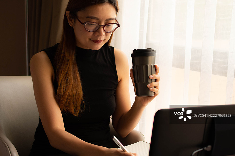 一位中年千禧一代的东南亚女性在家中使用笔记本电脑——通过用户友好的应用程序和平台检查余额、进行交易和管理预算。图片素材