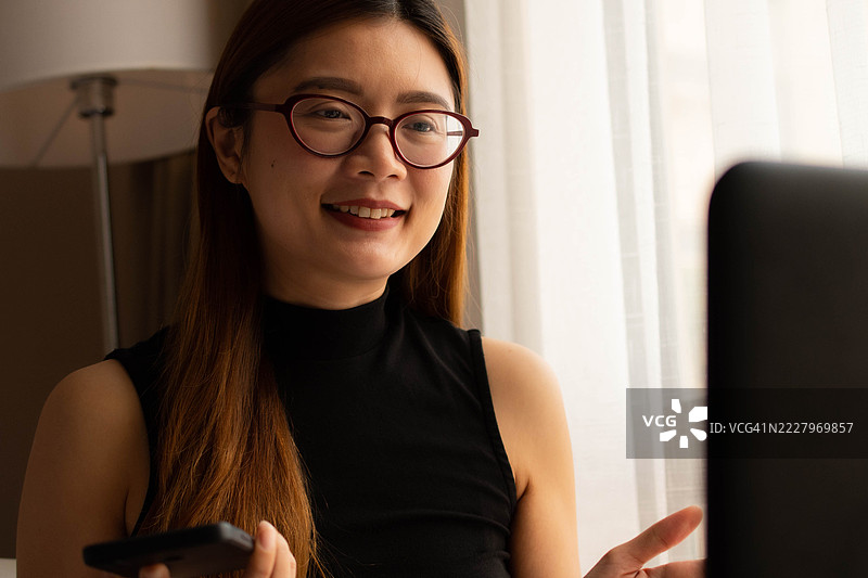 一位中年千禧一代的东南亚女性在家中使用笔记本电脑——通过用户友好的应用程序和平台检查余额、进行交易和管理预算。图片素材